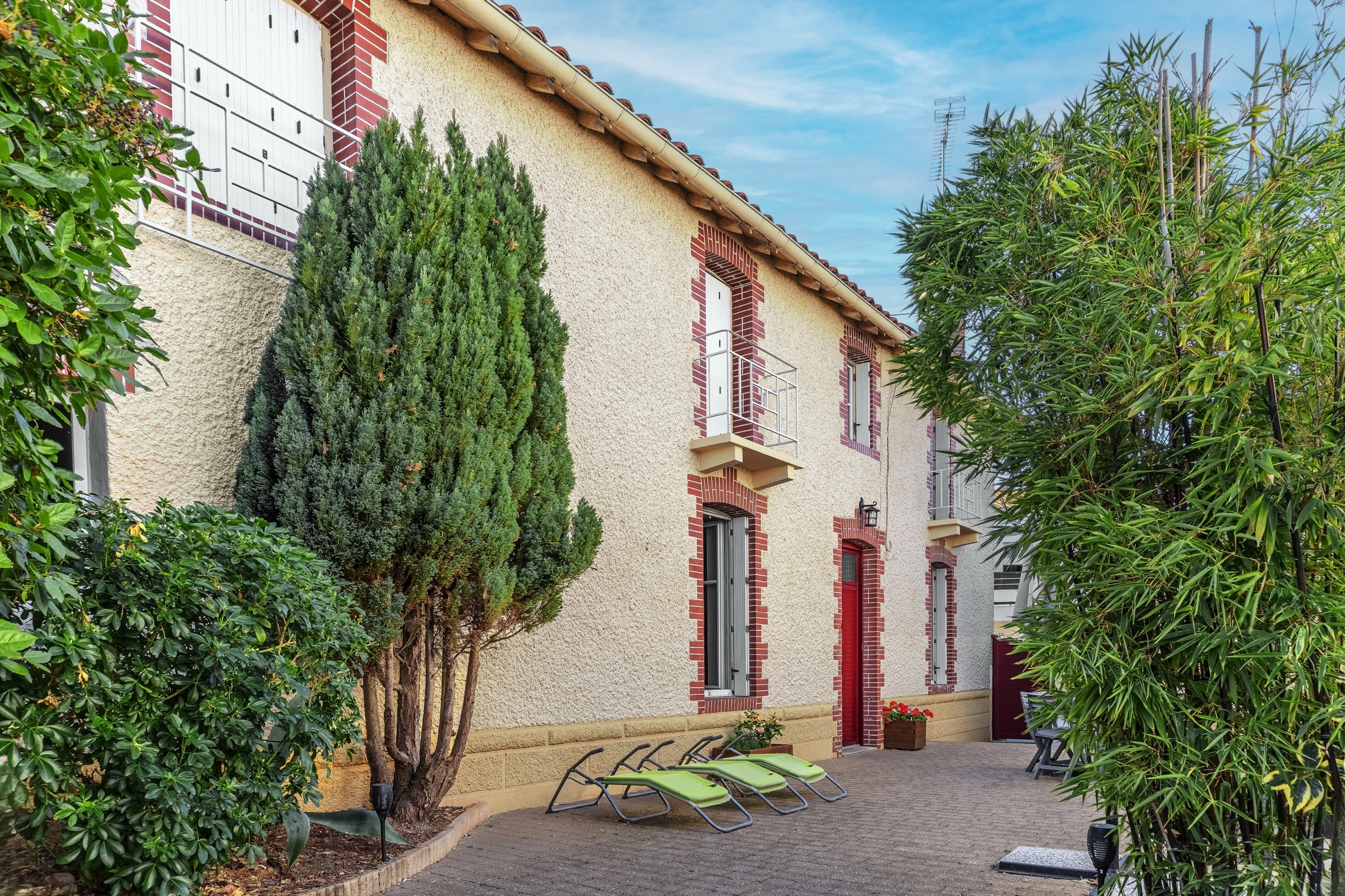 Façade en pierre et brique, jardin planté en premier plan